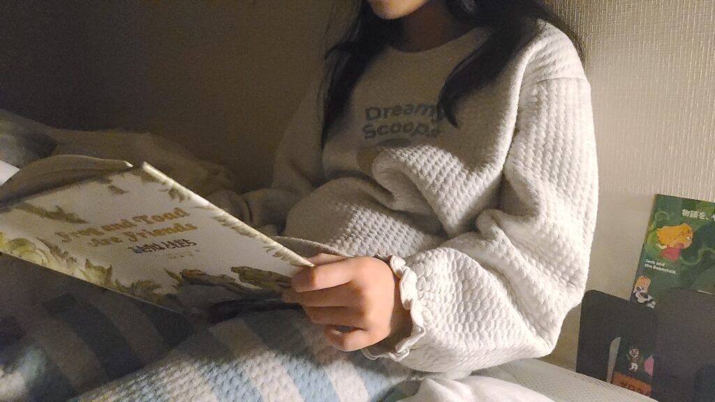 娘が寝室で英語絵本を見ている写真